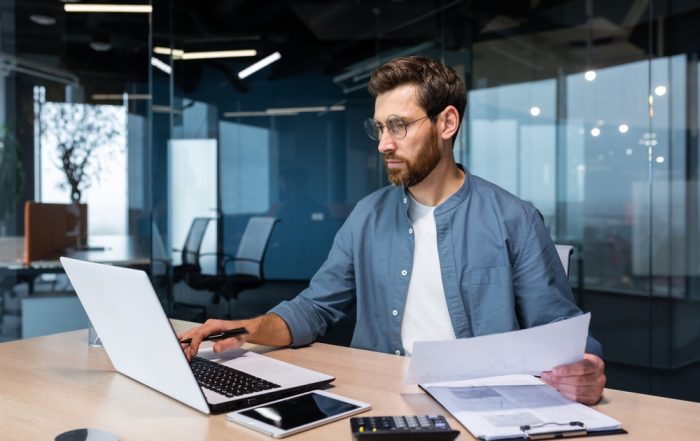Professional working on a laptop holding a piece of paper, illustrating case management and organisation