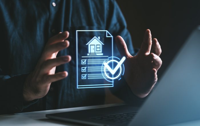 A person sitting at a desk with a laptop holds a glowing virtual document displaying a house icon, a checklist with ticked boxes, and a large check mark. The futuristic digital graphic represents property management, housing compliance, home inspections, or documentation processes.