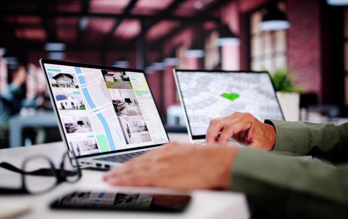 Estate agency professional reviewing online property listings and interactive maps on dual computer screens in a contemporary office environment.