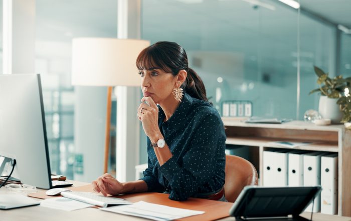 Office professional working at a desktop computer with documents on a desk in a modern workplace environment.